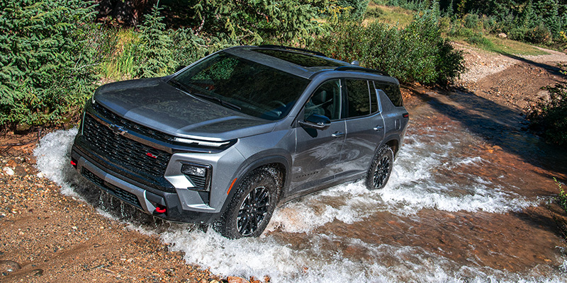 Gray SUV driving through shallow water on a rocky forest trail.
