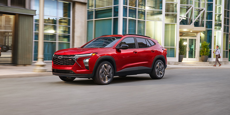 Red 2026 Chevrolet Trax driving through a modern city street.