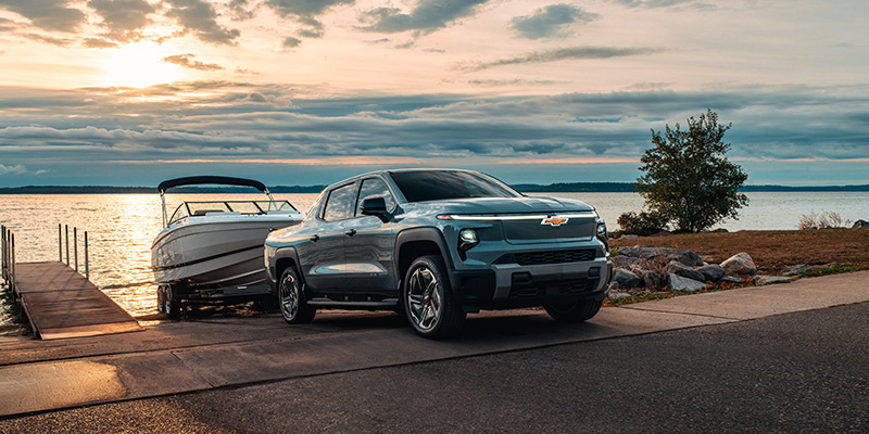 Light Blue 2026 Chevrolet Silverado EV Towing small boat from River